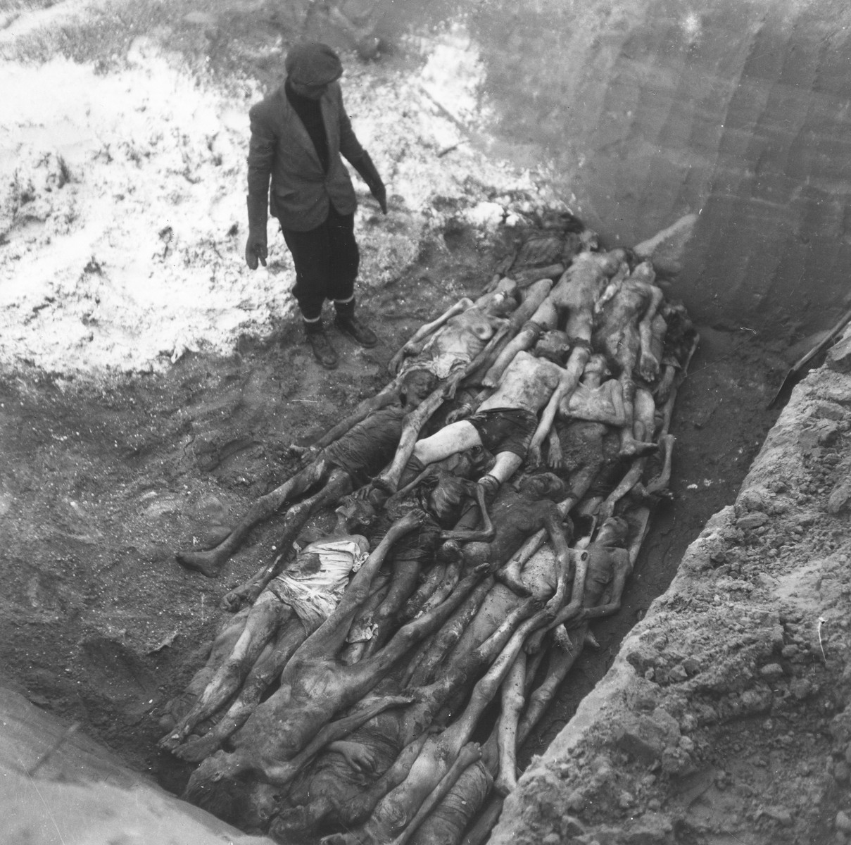 An undertaker views a layer of corpses laid out at the bottom of a mass grave in the Okopowa Street cemetery.  

Joest's caption reads: "Once again a layer of the dead was finished and now had to be covered with lime.  I couldn't believe one pit could have space for so many people."