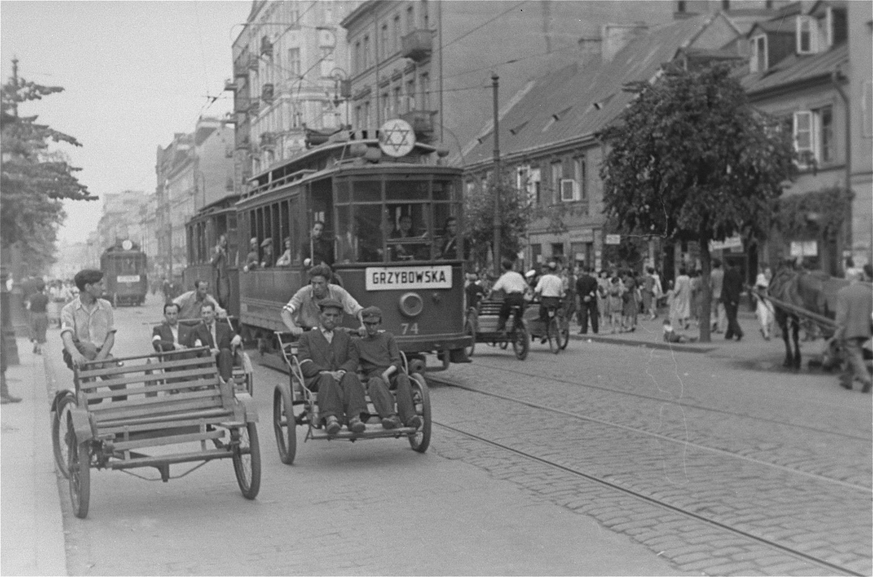 Rickshaws and streetcars move through a major street in the Warsaw ghetto.