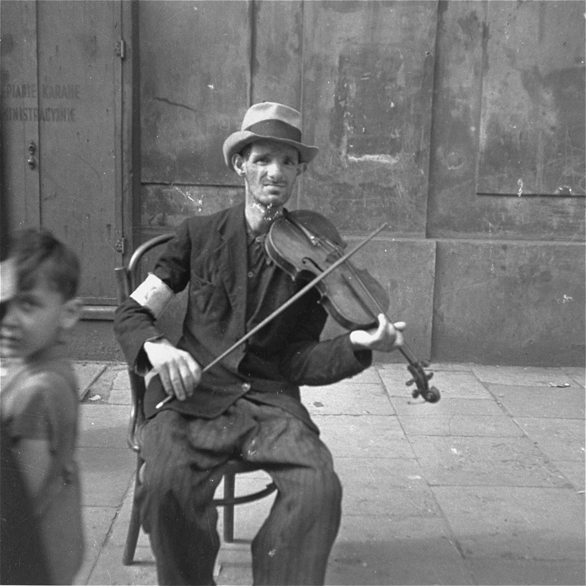 A man on the street plays the violin in the hope of receiving food or money.  

Joest's original caption reads:  "This man played the same sound on his violin again and again.  His eyes followed me, but whether out of fear or because he hoped to receive a coin I do not know."