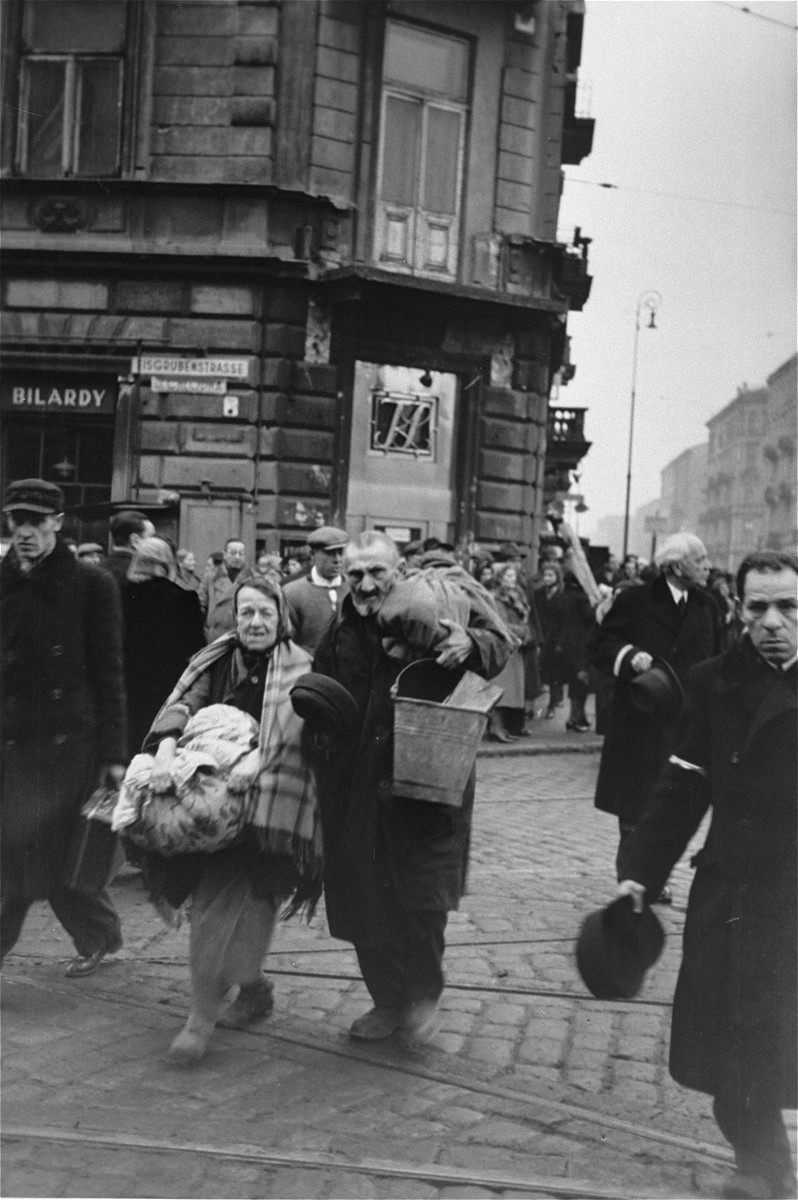 Jewish pedestrians crossing at the intersection of Chlodna and Zelazna Streets in the Warsaw ghetto, doff their hats to the German photographer.