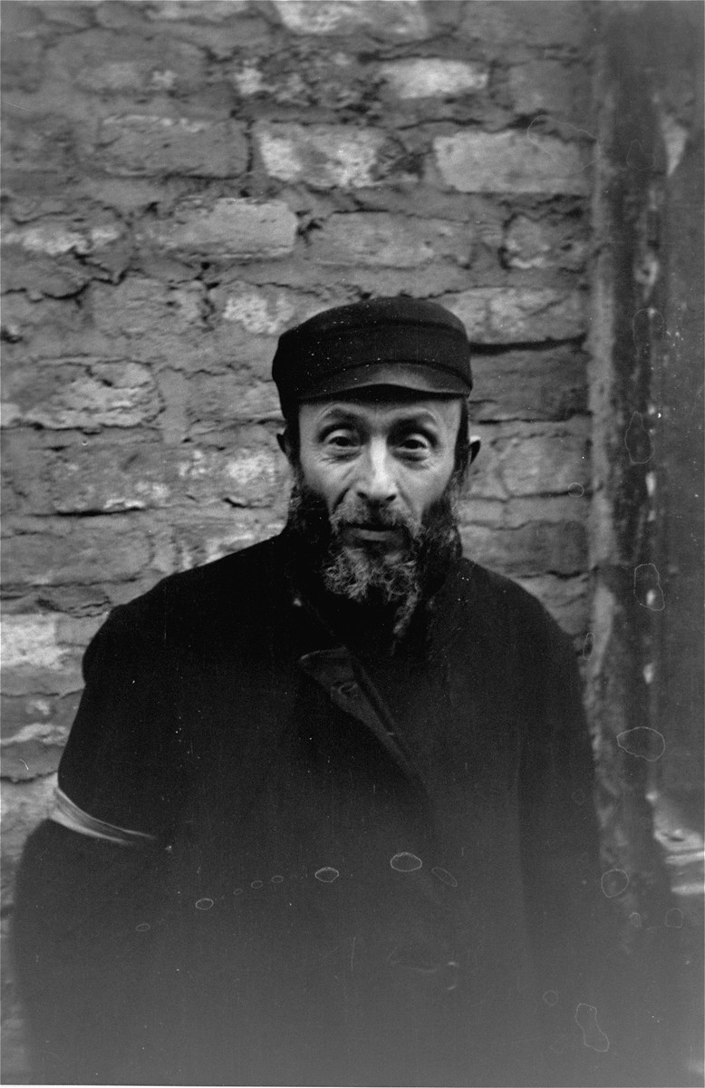 Portrait of a Jewish man standing in front of a brick wall in the Warsaw ghetto.