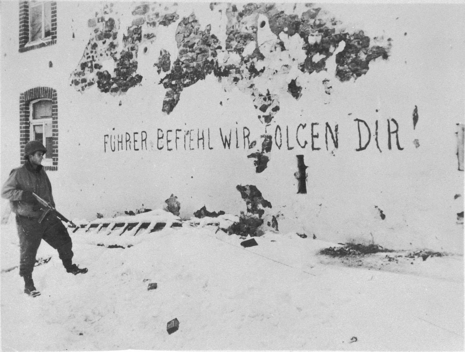An American soldier views a German slogan scrawled on the side of a building which reads: "Fuehrer give the order, we will follow."