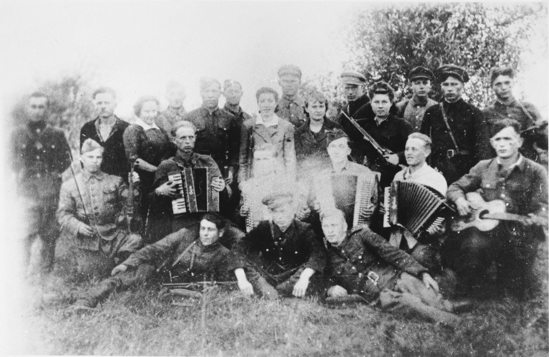 Group portrait of a Jewish partisan musical troupe in the Narocz Forest in Belorussia.  

Among those pictured are Hana Posner (standing in the back row, seventh from the left), her father, Mordechai Posner (fourth from the left) and Yechiel Burgin (sixth from the left).
