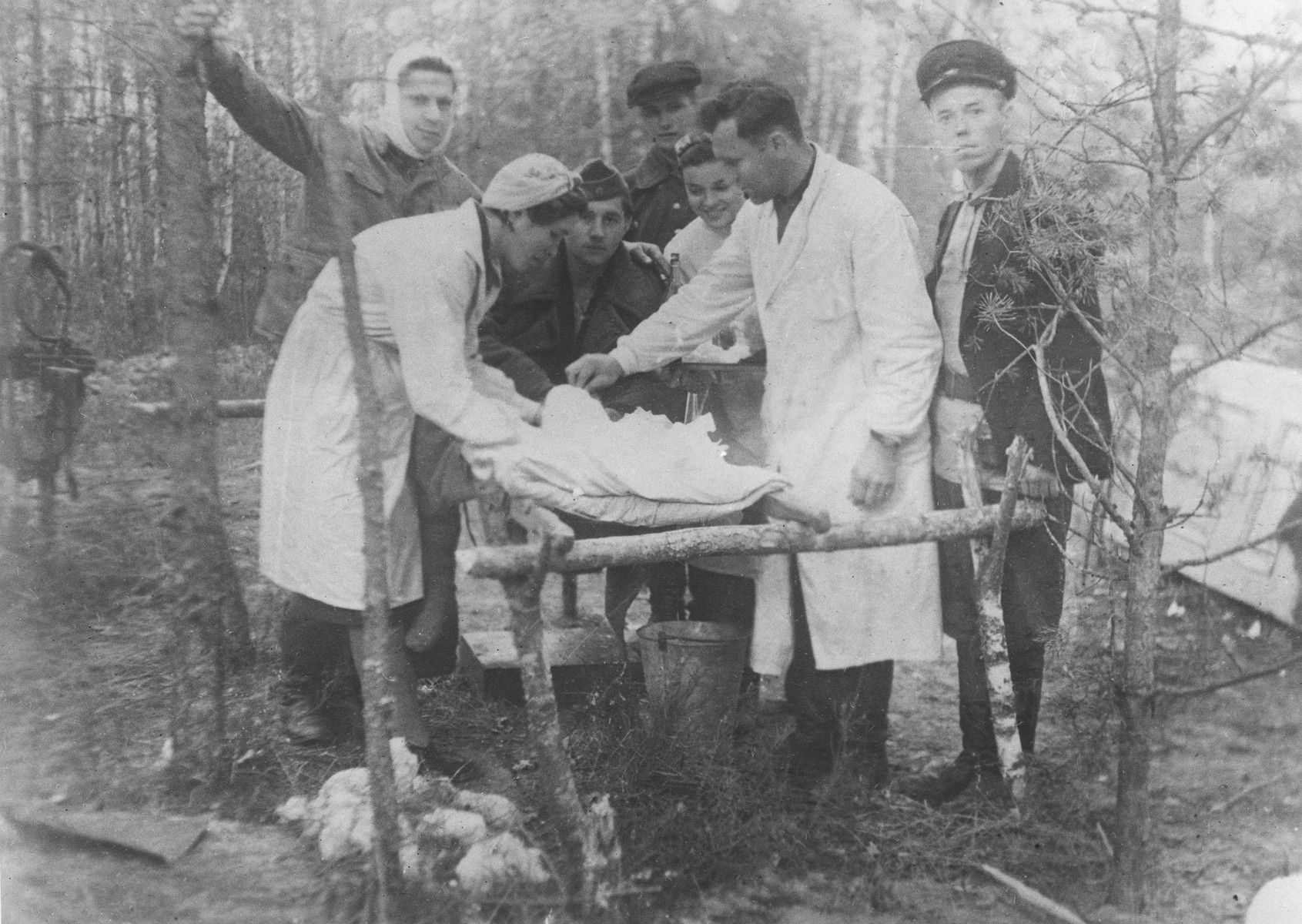 A wounded partisan is treated in a field hospital belonging to the Shish detachment of the Molotov brigade.

Among those pictured are Dr. Ivan Khudyakov, the brigade's physician (second from the right), and Fanya Lazebnik, a photographer and partisan nurse (left).  The wounded partisan's name is Sergei.