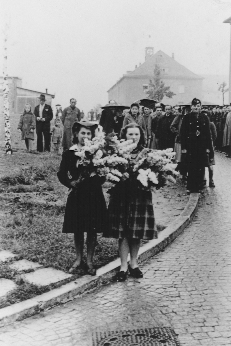 Two Polish women carry wreaths of flowers at a memorial observance after the war.  

Pictured on the right is Eve Kristine Vetulani.