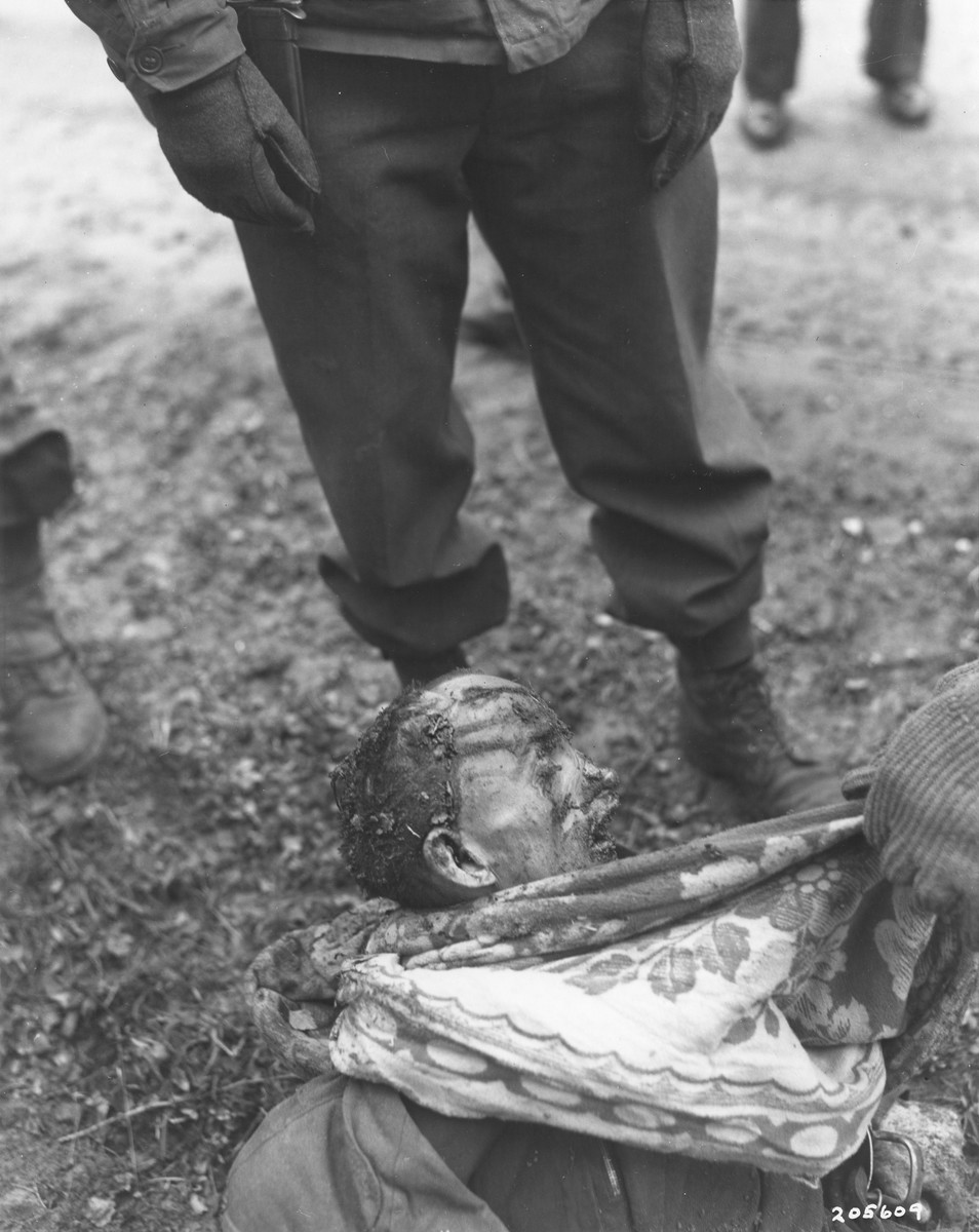 Members of the 97th Infantry Division, investigating war crimes, examin an exhumed body of a concentration camp prisoners who were killed by the SS while on a death march from Flossenbuerg.

The original caption reads "This is the body of one of the slave laborers killed during Death March from Flossenburg Concentration Camp near Weiden, Germany.  Many prisoners moved from Flossenburg to another camp as Allies advanced.  Those unable to march were shot and beaten, although suffering from malnutrition, by brutal SS guards.  Some bodies were exhumed during the investigation by Military Government of 97th Division, U.S. third Army."

By the beginning of April 1945, Allied forces were closing in on the Flossenbuerg concentration camp, which was situated 20 kilometers NE of Weiden, approximately five kilometers from the Czech border.  Several other concentration camps had already evacuated many of their prisoners to Flossenbuerg earlier in the year, including Buchenwald and Auschwitz, so that by the beginning of May the camp and its satellites were overflowing with almost 52,000 prisoners.  Now, because the area was also about to be liberated, a series of evacuation transports was sent southwest by train in the direction of Dachau.  Allied planes already active in the area had successfully destroyed a number of rail lines and locomotives, effectively delaying many of the transports, or forcing them to take alternate routes.  A number of the trains laden with prisoners were even fired on while in transit, accidentally killing prisoners.  Eventually, most of the prisoners were forced to continue their journey on foot because of the destruction to the German rail system.  During these “death marches,” numerous prisoners were killed by the SS for lagging behind or stumbling.  When ammunition ran short after several days of marching, the slower and weaker prisoners were beaten to death rather than shot.  Some of the bodies were buried by prisoners who were kept at the back of the group for exactly this purpose.  Others were just left on the side of the road.