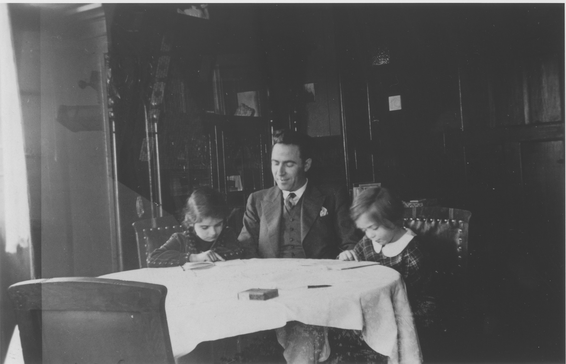 A Jewish religion teacher tutors two young girls in the dining room of a private home in Guntersblum, Germany.

Pictured from left to right are Ann Hellman, Carl Hartogsohn and Inge Seeman.