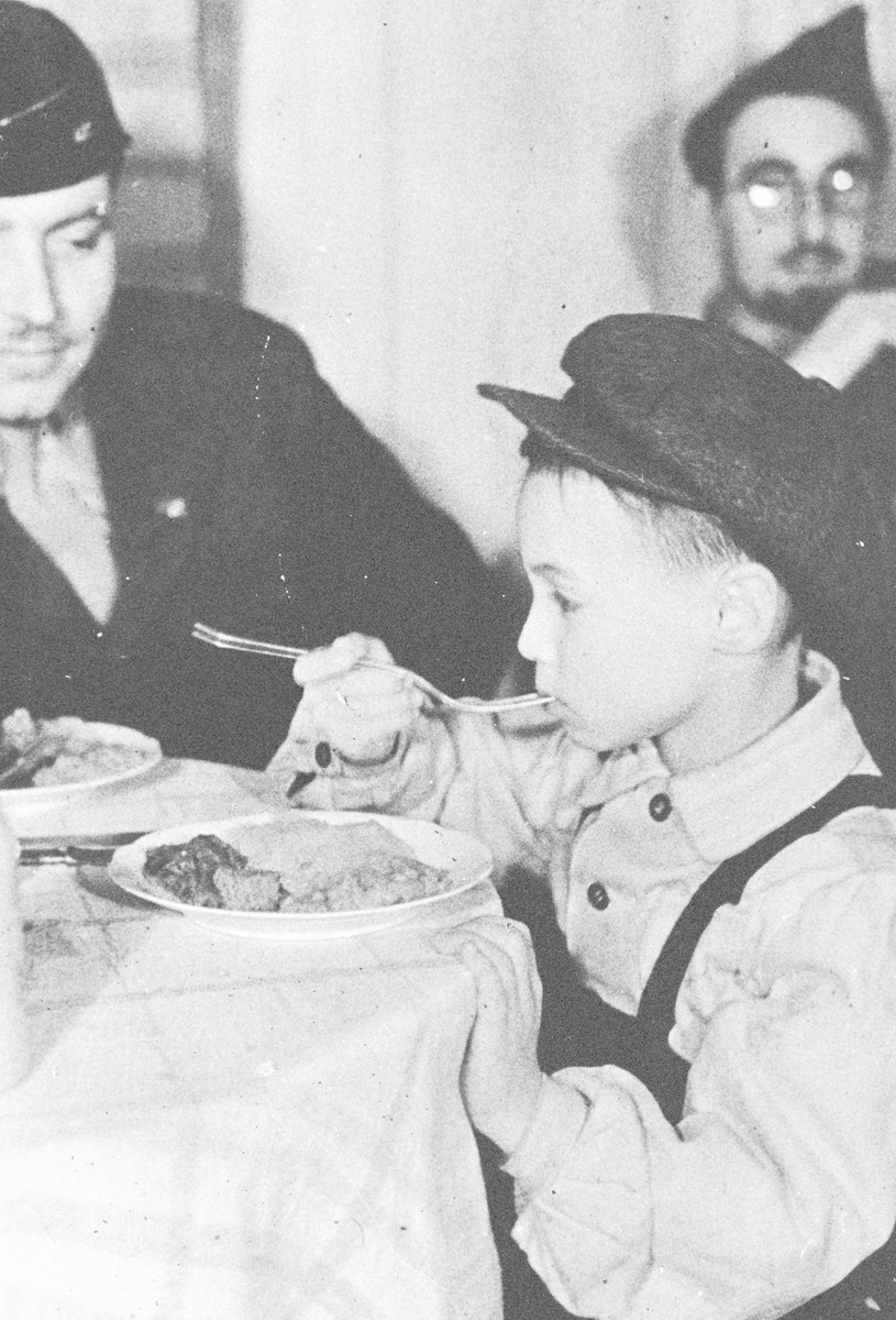 Rabbi Nathan Baruch and Rabbi Aviezer Burstein watch a young child eat at the kosher kitchen in the Dachau displaced persons' camp.
