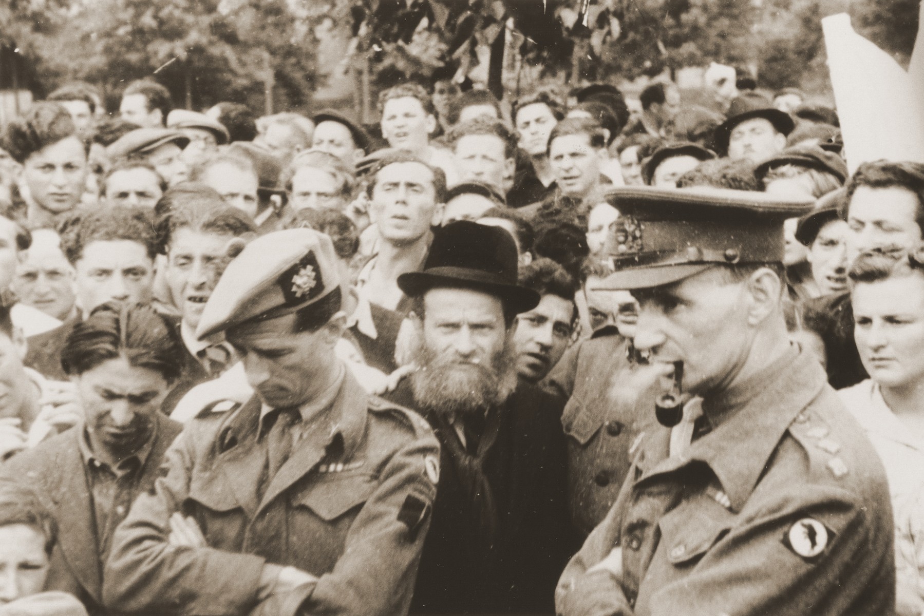 A crowd of Jewish DPs stand behind British soldiers at a ceremony or demonstration in the Bergen-Belsen displaced persons camp.