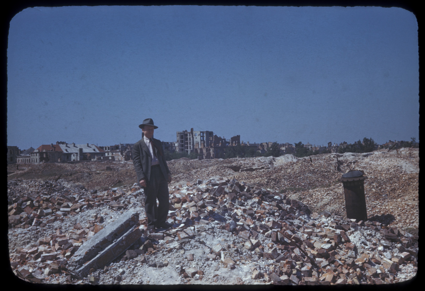 Postwar view of the ruins of the Warsaw ghetto, with a man standing in the foreground.