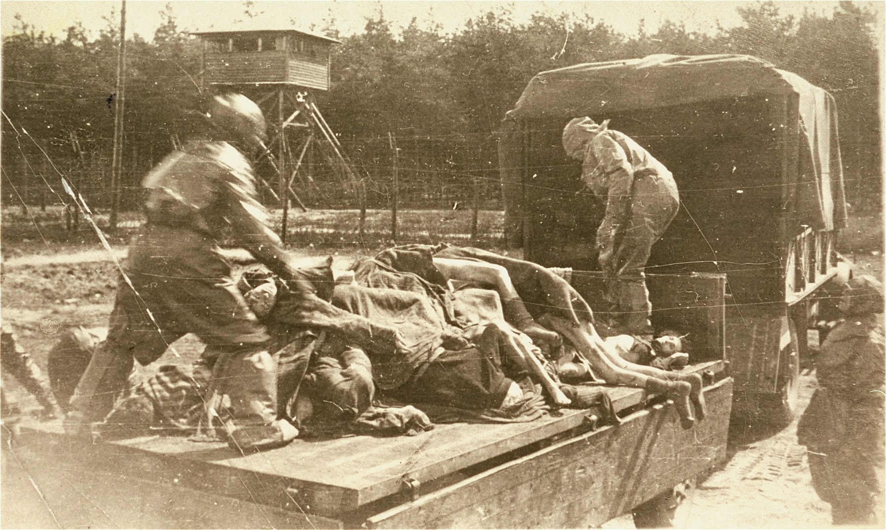 Personnel dressed in protective garb load corpses onto the back of a truck.