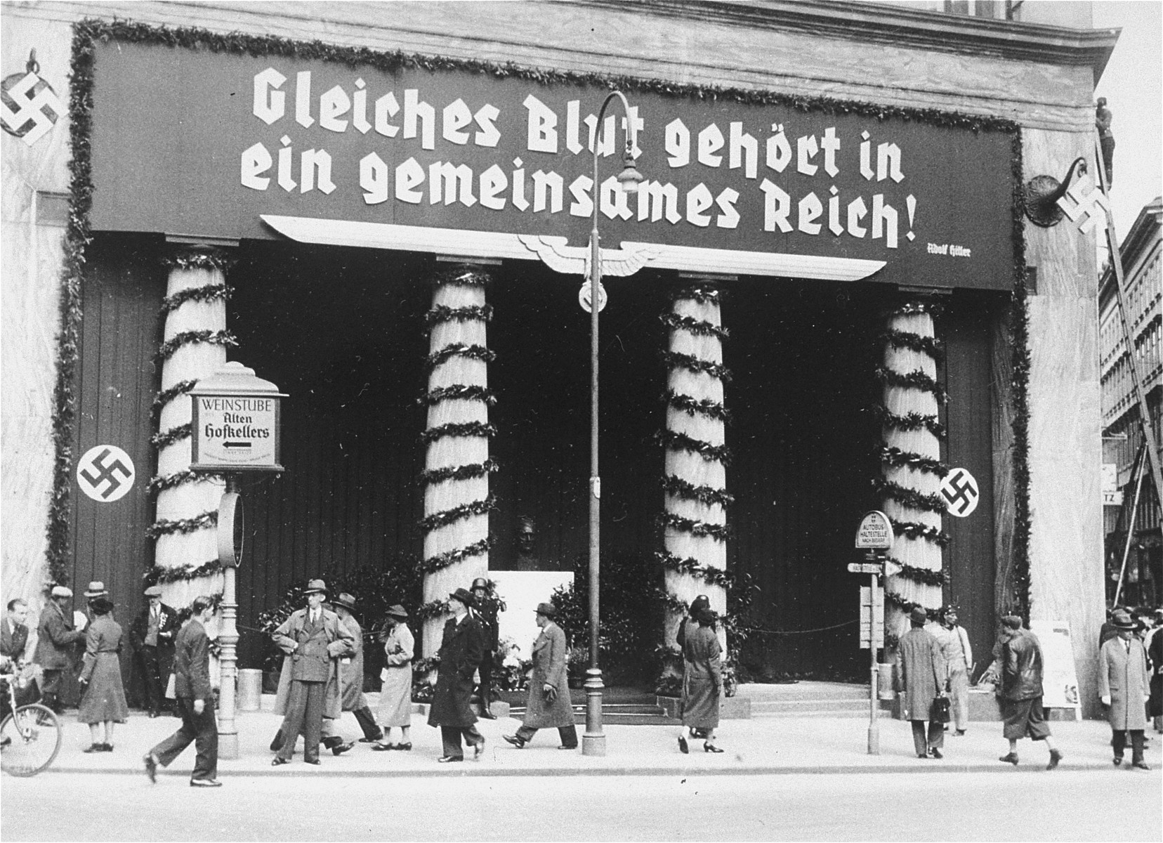 View of the Loos Haus, a public building in Vienna, adorned with decorations and a large banner bearing a quote from Hitler, "Those of the same blood belong in the same Reich!"  

Such banners were hung throughout Austria in the weeks preceding the April 10th plebescite on the incorporation of Austria into the German Reich.