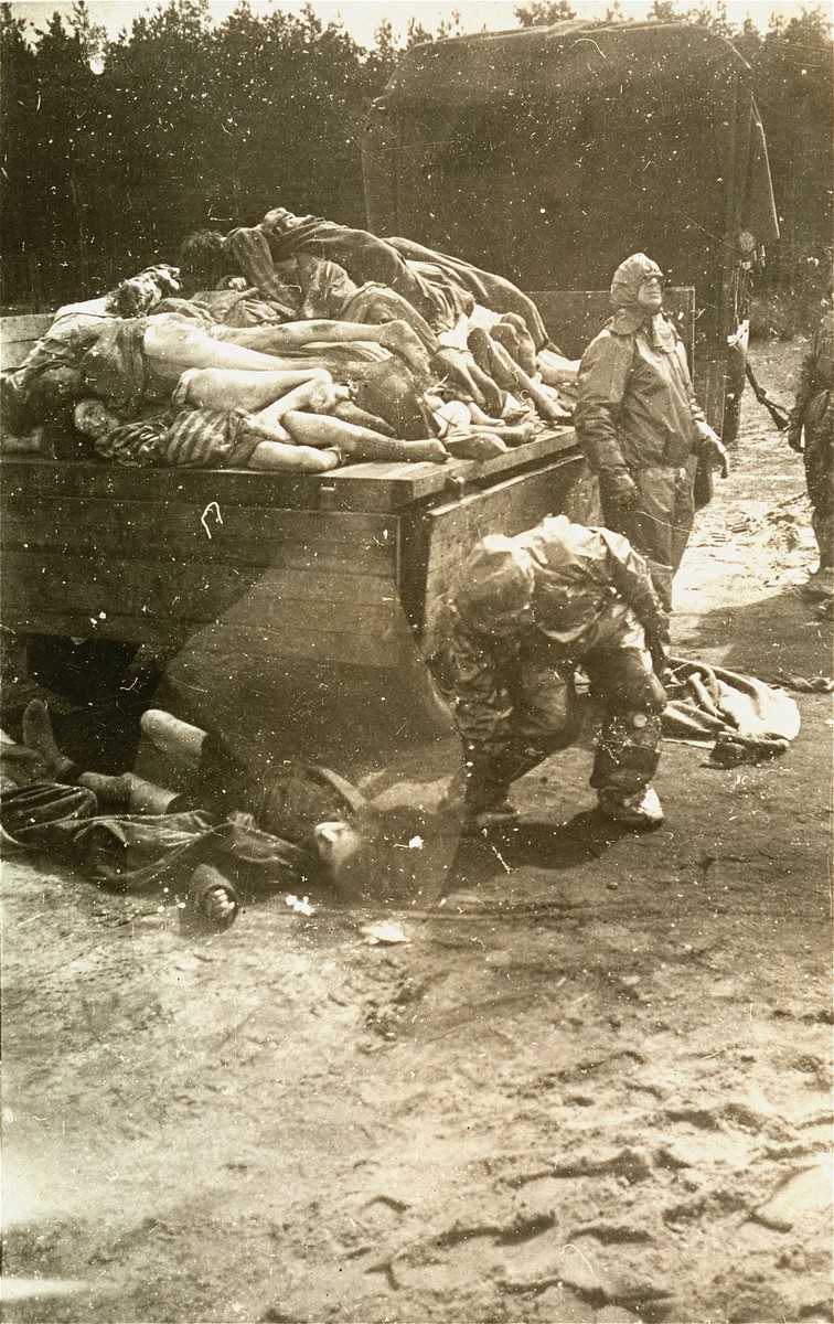Personnel dressed in protective garb load corpses onto the back of a truck.