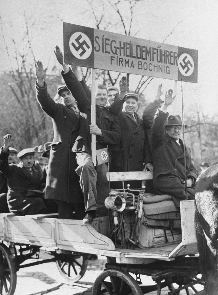 Employees of the Firma Bochig, holding a wooden sign "Sieg Heil to the Fuehrer," give the Nazi salute from their horse-drawn wagon.  They are among the Viennese celebrants who have come to welcome the arrival of German troops into the city.