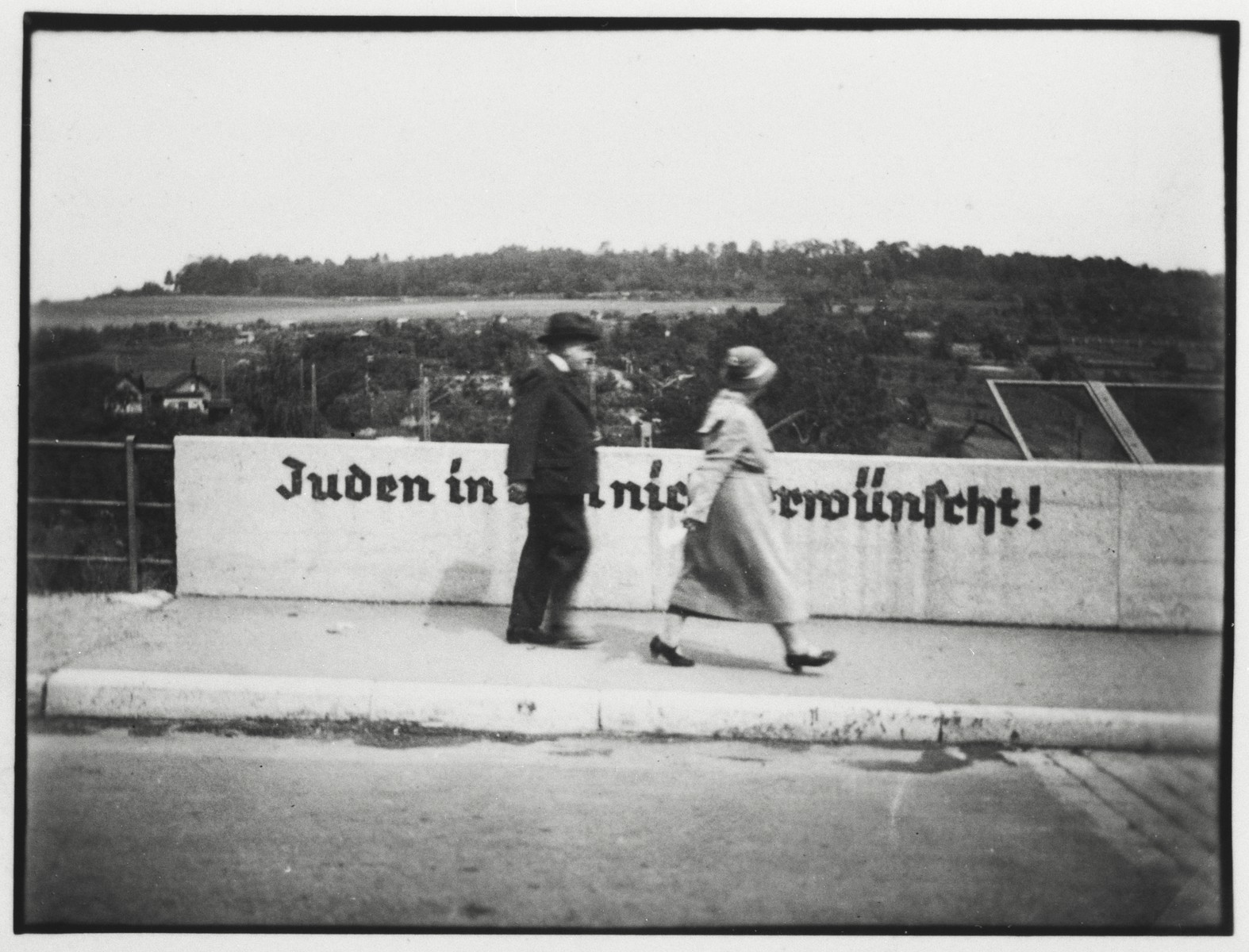 A Jewish gentleman and his daughter cross the Stuttgarter Strasse bridge in Ulm that is painted with the sign "Jews are not desireable in Ulm".

Pictured are Jacob Guggenheimer and Irene Guggenheimer Einstein (the grandfather and mother of the donor).