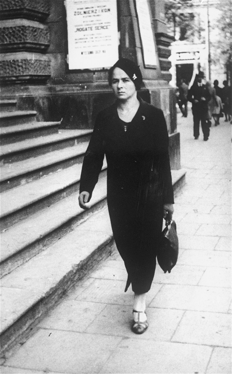 A young Jewish woman walks along a commercial street in Warsaw, Poland.

Pictured is Yona Rudashevsky, the aunt of donor Cilia Rudashevsky.  Yona studied nursing in Vilna and then worked in a Jewish hospital in Warsaw.  In 1935 she immigrated to Palestine, where she worked as a nurse in the Belinson hospital.