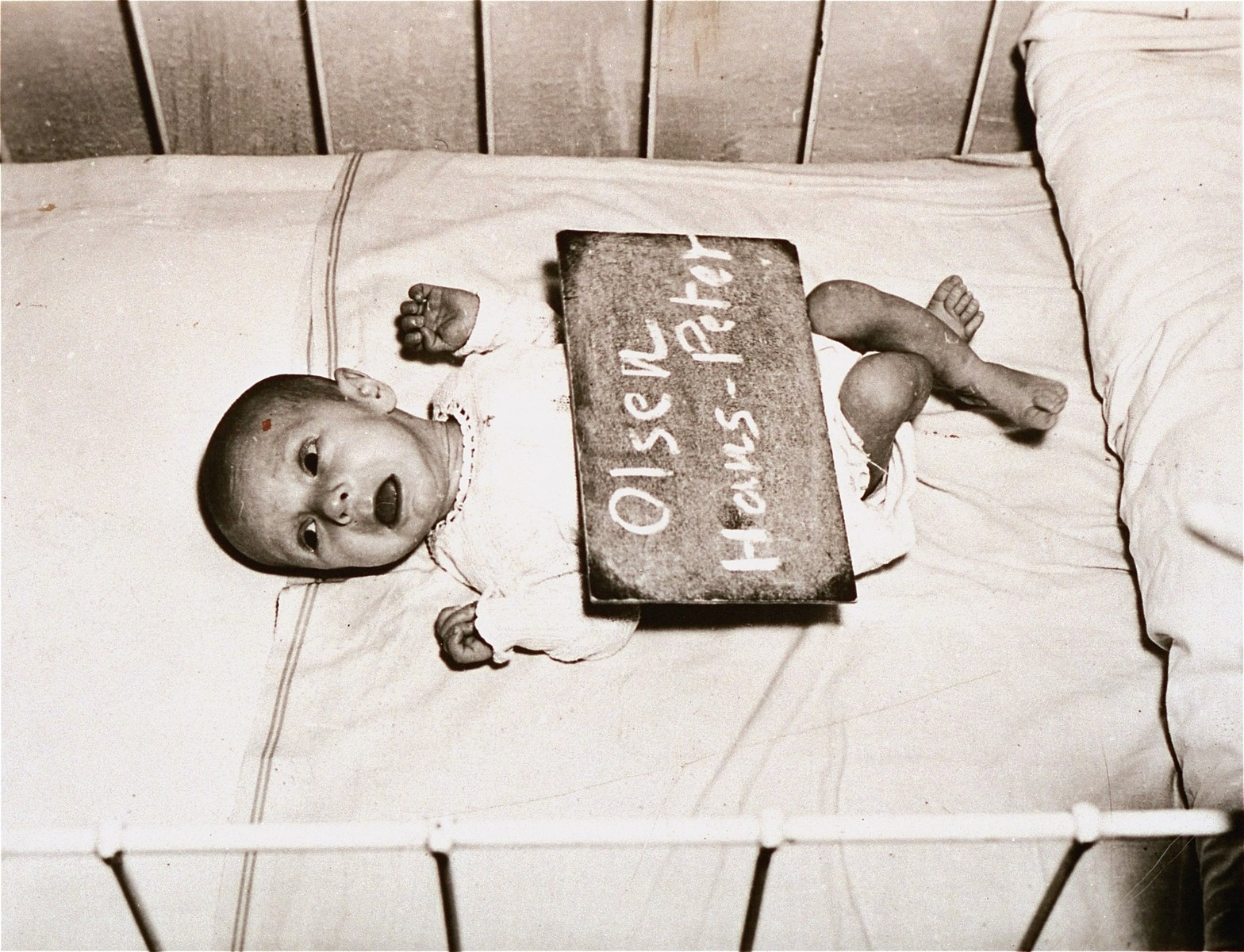 Infant Hans-Peter Olsen with a name card intended to help any of his surviving family members locate him at the Kloster Indersdorf DP camp.  This photograph was published in newspapers to facilitate reuniting the family.