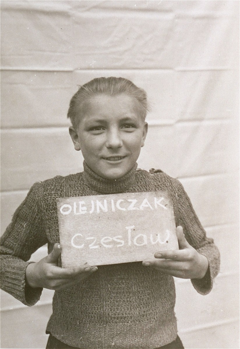 Czeslaw Olejniczak holds a name card intended to help any of his surviving family members locate him at the Kloster Indersdorf DP camp.  This photograph was published in newspapers to facilitate reuniting the family.