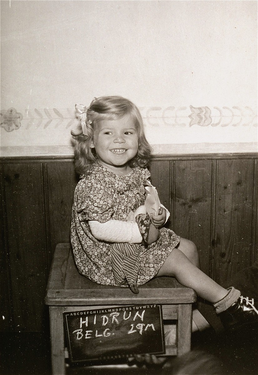 Belgian child Hildrun de Maere, surname unlisted, poses with a name card intended to help any of her surviving family members locate her at the Kloster Indersdorf DP camp.  This photograph was published in newspapers to facilitate reuniting the family. 

She was adopted in America.