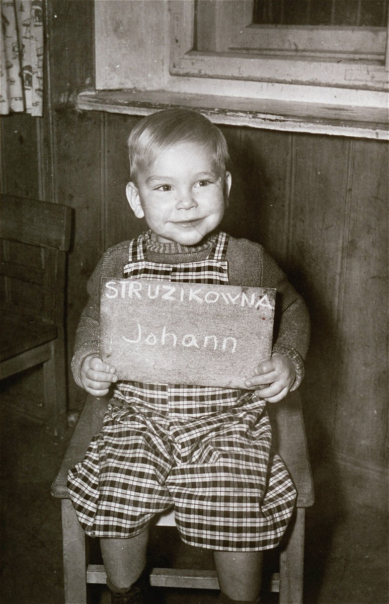 Johann Struzikowna holds a name card intended to help any of his surviving family members locate him at the Kloster Indersdorf DP camp.  This photograph was published in newspapers to facilitate reuniting the family.
