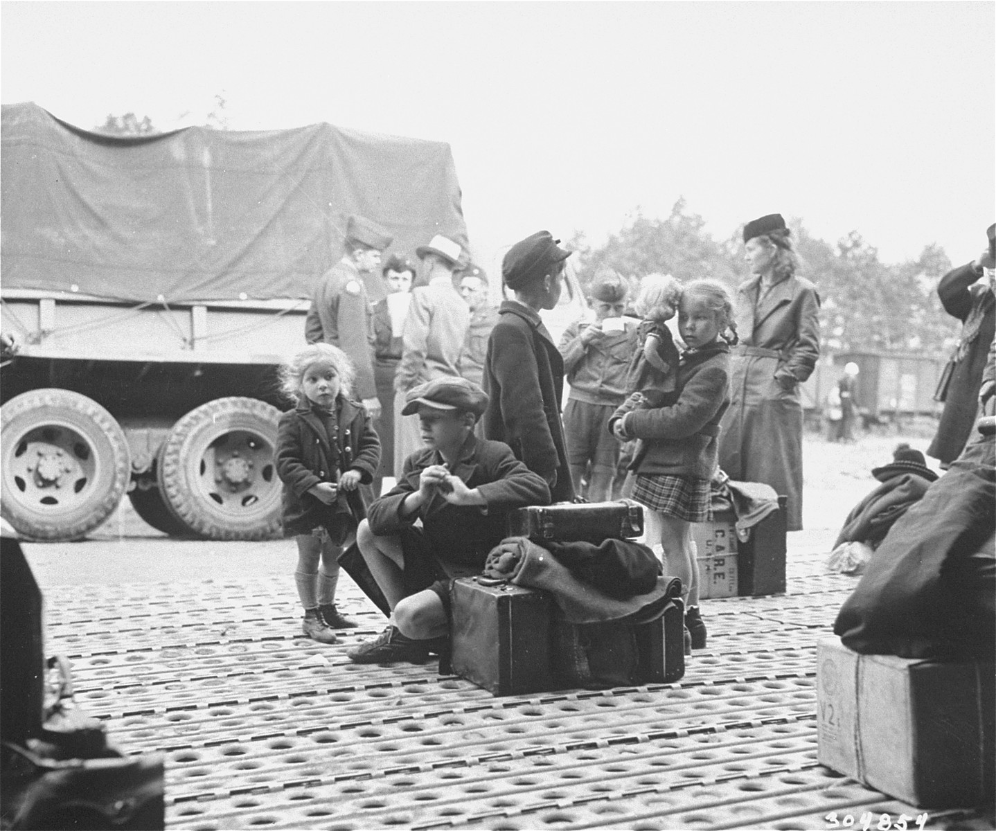 Jewish DPs who have been evacuated from Berlin to Frankfurt as a result of the Soviet blockade, wait at the Rhine Main Airfield for transport to displaced persons camps.

The original caption reads, "Jewish displaced persons arrive by plane at the Rhine Main Airfield, Frankfurt, Germany, from the blockaded city of Berlin, on operation "Vittles".  150 came in the first group, and 180 are expected to arrive on July 24, 1948. Most of these DPs have been granted visas by the new State of Israel, and will go to DP camps in the U.S. zone to await shipment to Palestine, while others will leave for Canada, France and the U.S.. Here DPs wait for trucks to arrive to carry them to trains."