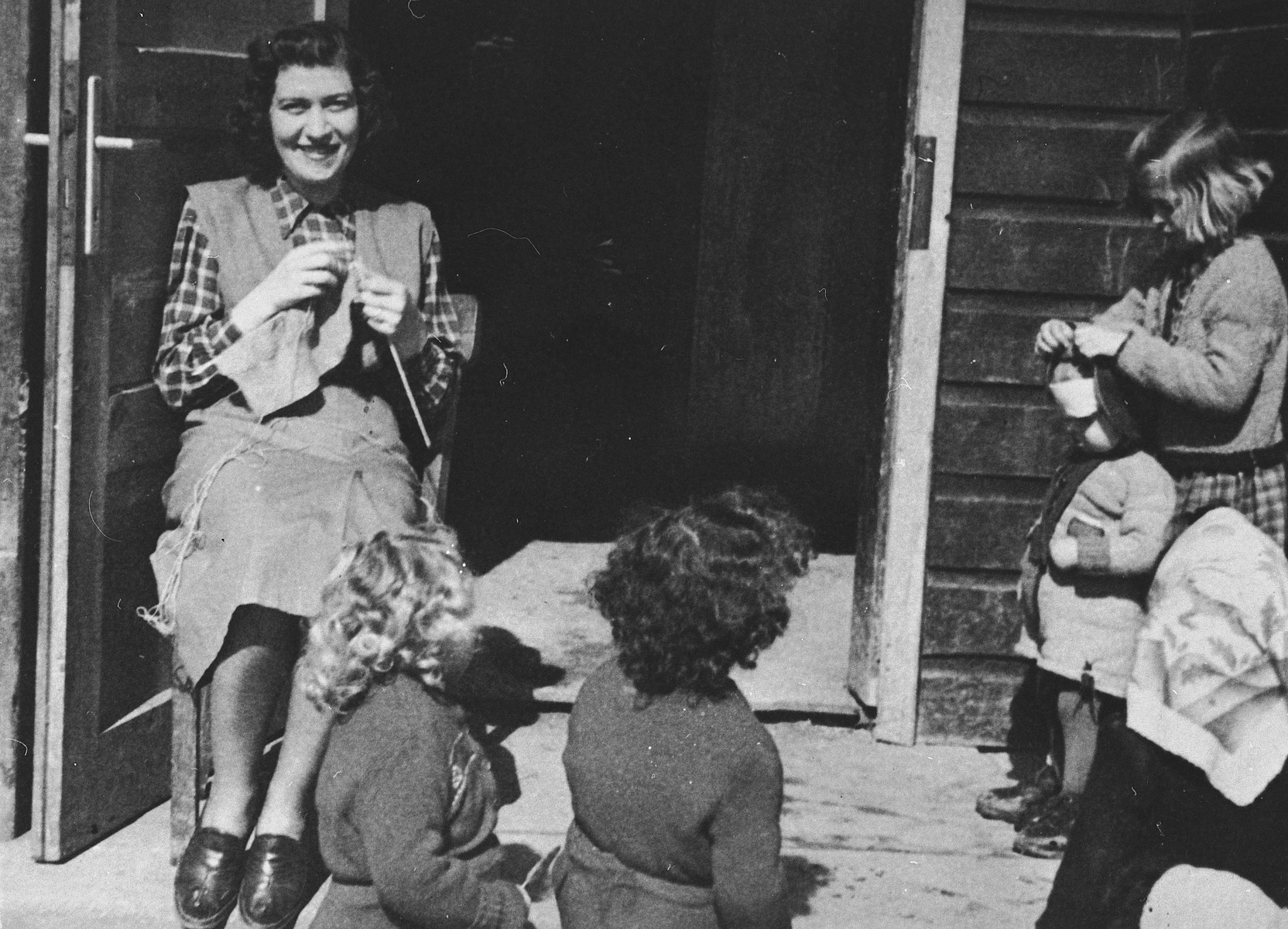 A young woman knits while watching a group of preschoolers in the Wels DP camp.