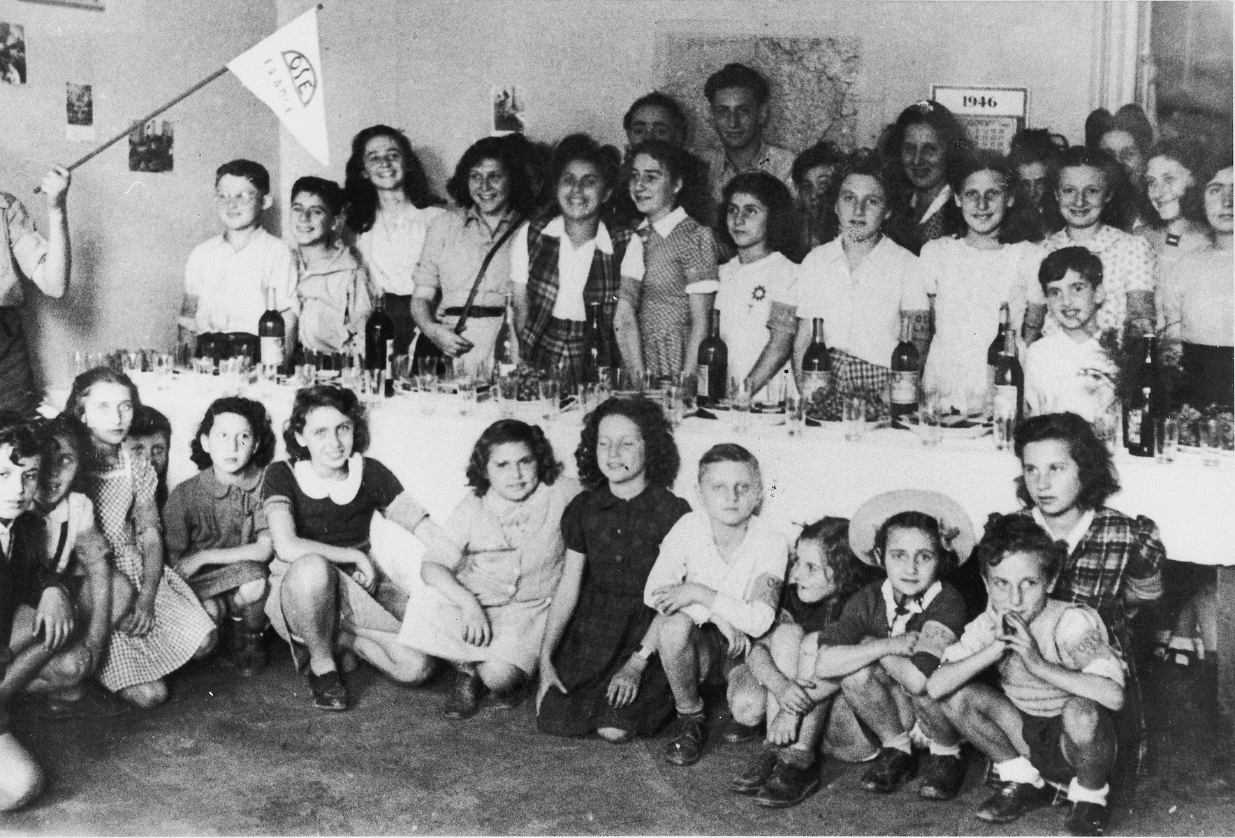 Children gather around a festive table set with wine and wine cups in an OSE home in France.

Among those pictured is former St. Louis passenger, Judith Koeppel.