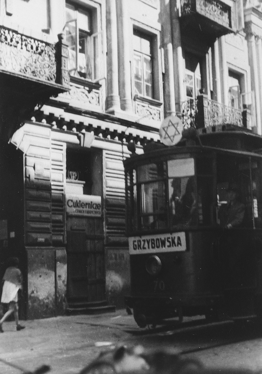 A streetcar marked with a large Star of David rides down a street in the Warsaw ghetto.

The sign on the front of the car says Grzybowska.