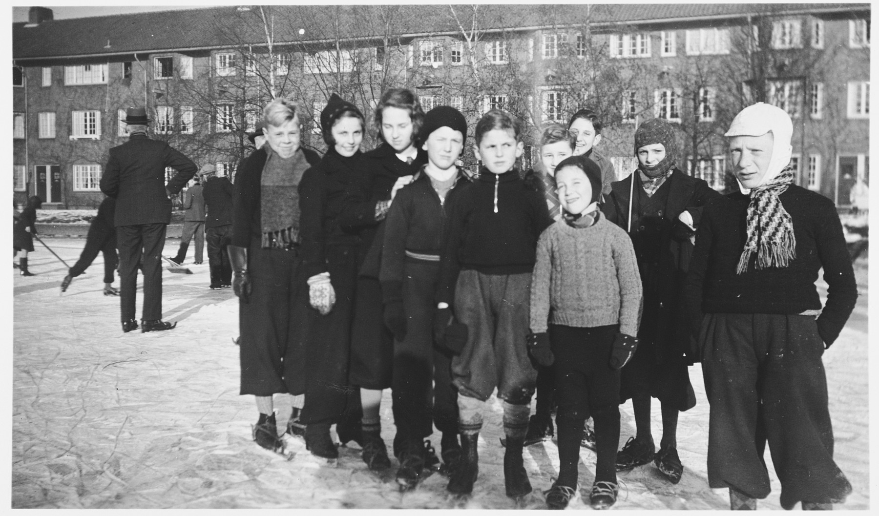 Group portrait of school children on an ice skating rink in Amsterdam.

In the background children involved in a game of curling.