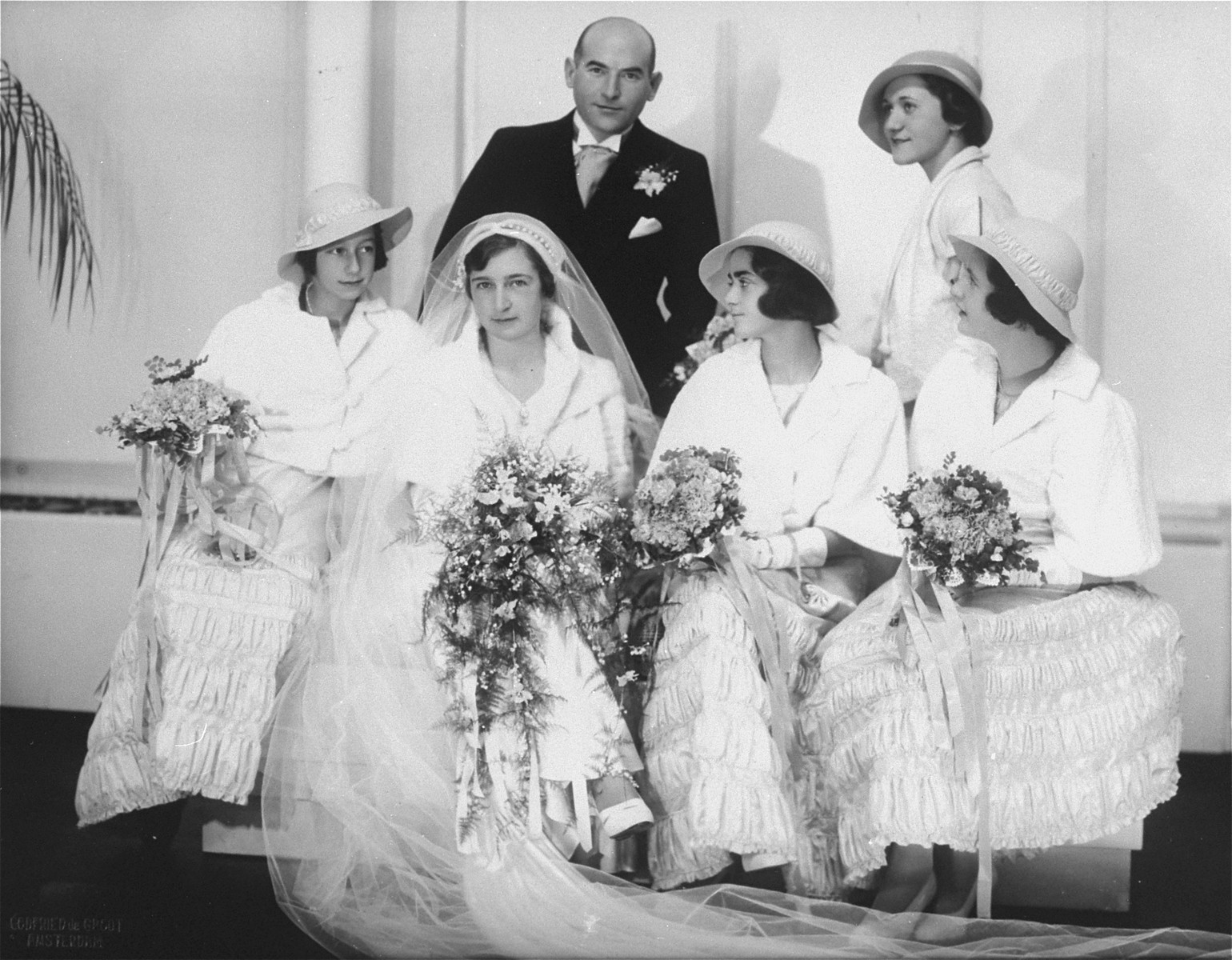 Group portrait of Hilde and Gerrit Verdoner with four bridesmaids on their wedding day.  

Pictured from left to right are: Jetty Fontijn, Hilde Verdoner, Letty Stibbe, and Miepje Sluizer; standing behind them is Fanny Schoenfeld.