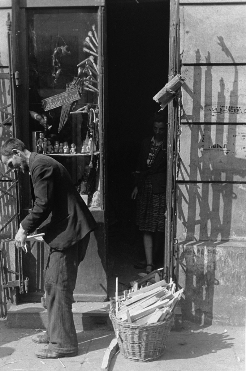 A vendor selling kindling stands in front of a store that specializes in the repair of umbrellas and dolls.