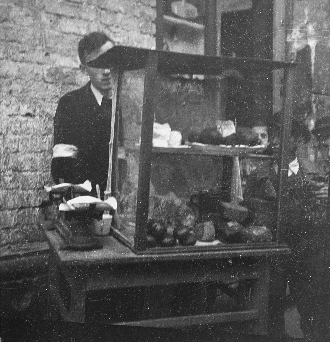 A vendor on the street in the Warsaw ghetto offers bread and cheese for sale. 

Joest's original caption reads: "This man sold bread and cheese on the street.  Children surrounded his glass case, but could not buy anything."