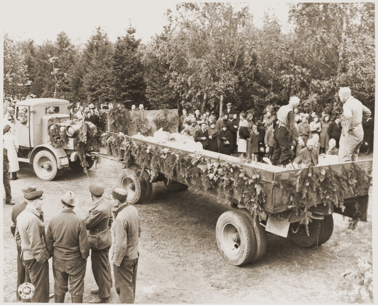German civilians load the bodies of Soviet prisoners of war wrapped in sheets onto a semi-trailer.  

The prisoners were exhumed from a mass grave in Wuelfel and will be reburied near the Hanover City Hall.

On April 8, 1945, 200 Red Army officers and other prisoners of war were sent on a death march from the Liebenau labor camp, 50 kilometers NW of Hanover, where the prisoners worked in a munitions factory.  As they reached Wuelfel, a suburb of Hanover, the SS guards ordered 25 prisoners, including one woman, to dig a large grave.  While this was being done, a prisoner killed a guard with a shovel and was able to escape to the woods nearby.  From there he heard the shots as the remaining prisoners were killed and buried in the grave.  Several weeks later, as American troops swept through the area, the mass grave was discovered.  On May 2, the 35th Division of the U.S. Ninth Army gathered townspeople from Wuelfel and forced them to exhume the grave, wrap the bodies in sheets, and rebury them near the Hanover City Hall.  Before reburial, many of the victims were identified by friends and relatives remaining in the area.