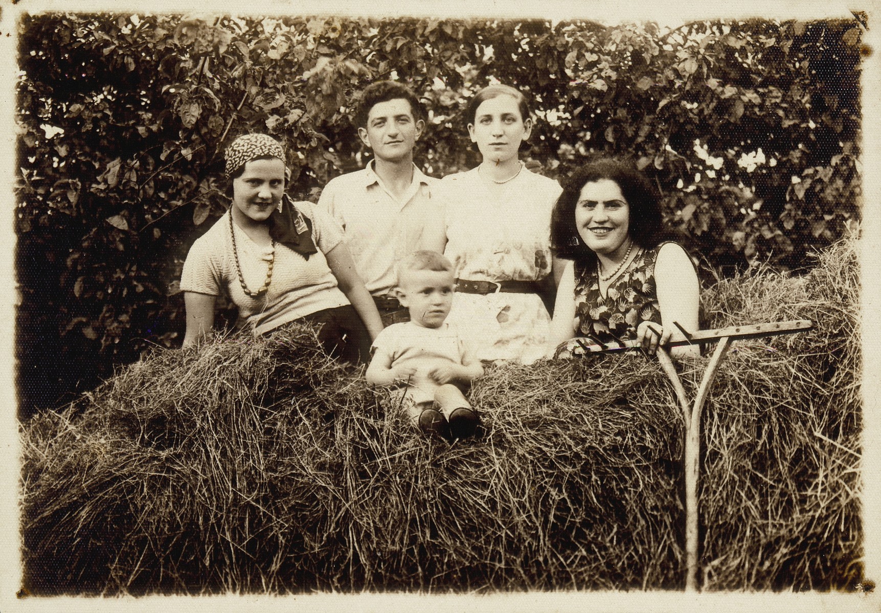 Four young people and a young baby sit on top of a hay wagon. 

(right to left) Miriam Koppelman Rushkin, an unidentified visitor, Shepske Sonenson, Malka Nochomowicz, and baby Elisha Rushkin.  Miriam died a natural death; all the others were killed by the Germans during the September 1941 mass shooting action in Eisiskes.