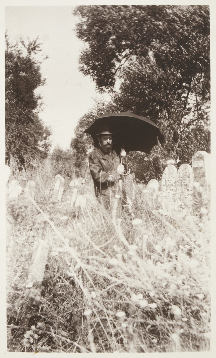 Rabbi Hertz Mendl (Naftali Menachem) Hutner, carrying an umbrella, guides visitors through the Eisiskes' cemetery.