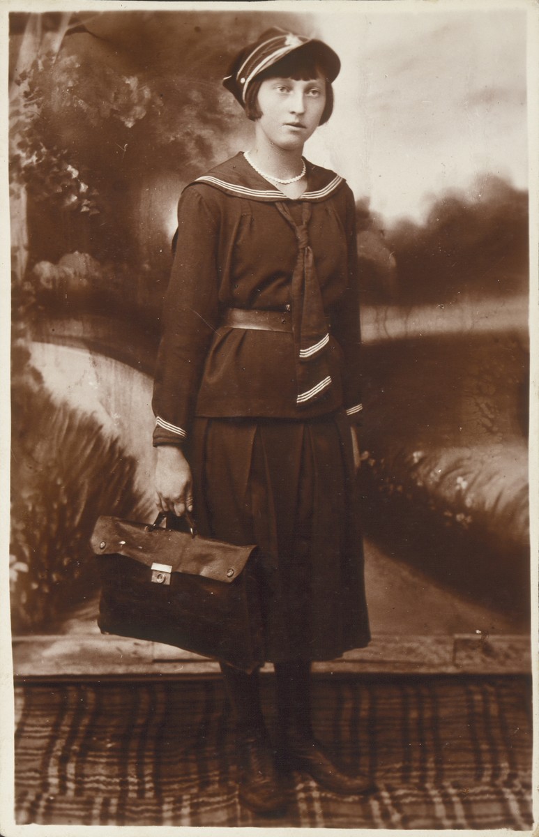 Shoshana Katz, wearing her high school uniform and carrying a brief case, poses for a studio portrait . 

Shoshana was the daughter of Alte and Yitzhak Uri Katz, the shtetl's  photographers and pharmacists. She was killed by the Germans during the September 1941 mass shooting action in Eisiskes.