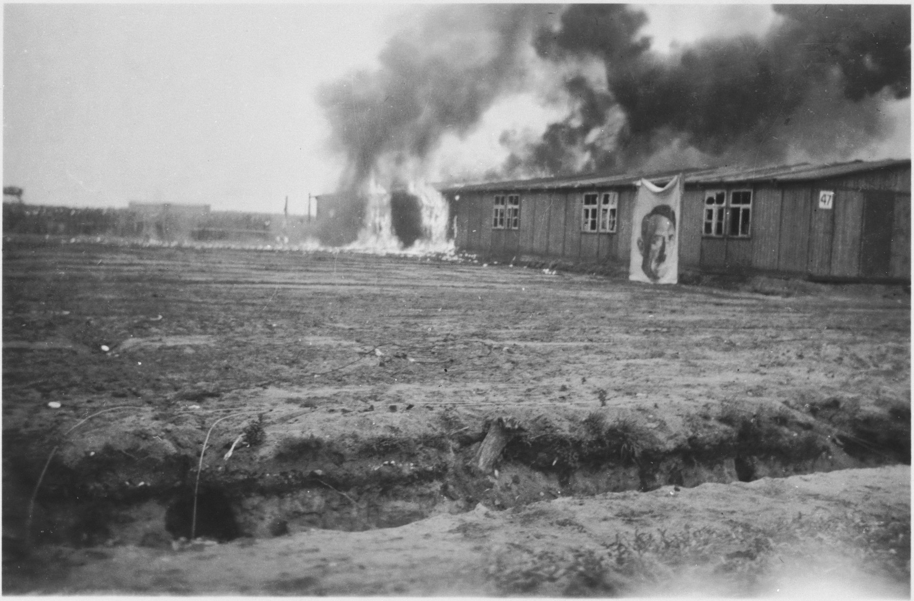 Fire consumes a barracks in the Bergen-Belsen concentration camp decorated with a wall size portrait of Adolf Hitler.  

The barracks were burned to control the spread of epidemics.