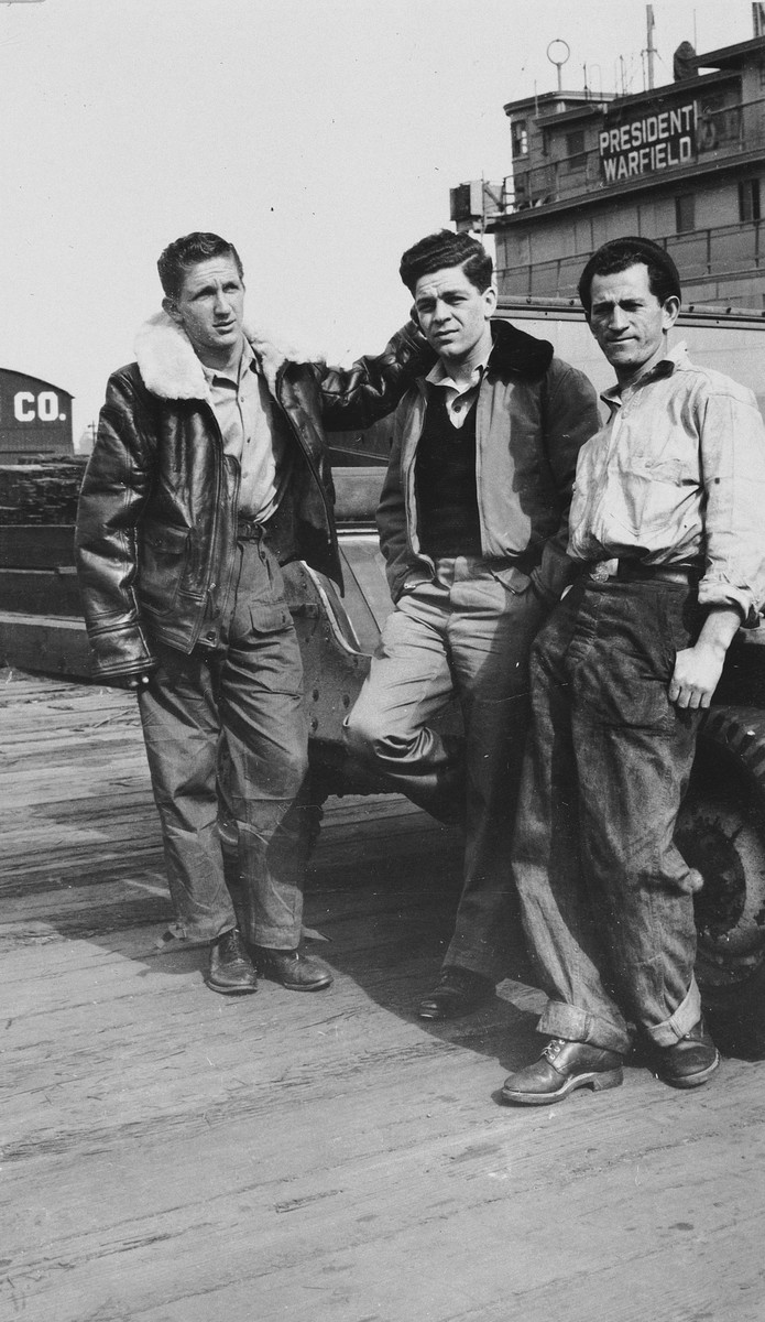 Three crew members pose on the pier in front of the President Warfield (later the Exodus 1947) in Baltimore harbor.

Pictured in the center is Avi Livney.  He is flanked by two Mexican crew members, Reuben Margolis (left) and Avraham Siegel (right).