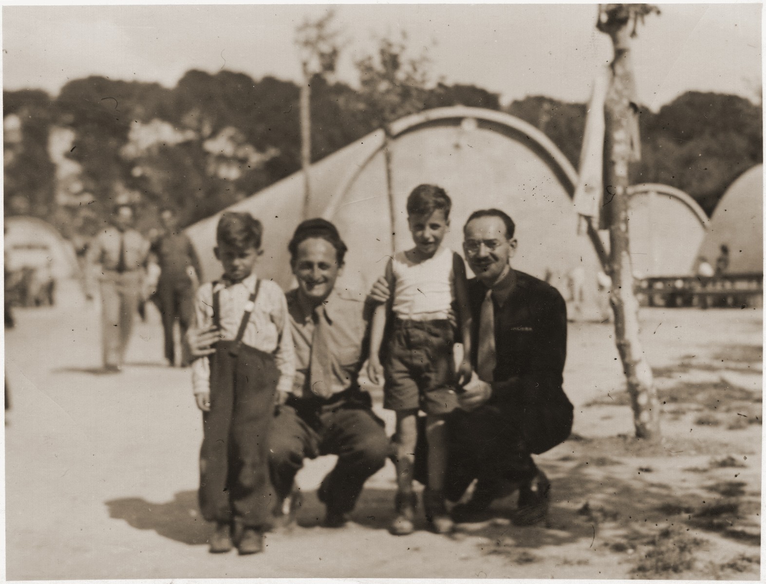 Two Jewish orphans pose with two relief workers at the Marsylia transit camp (a former Yugoslav POW camp) in Marseilles, where they await their departure for Palestine aboard the SS Champollion.  

The two boys belong to a group from the Bergen-Belsen displaced persons' camp who have been selected for the first authorized children's transport to Palestine.