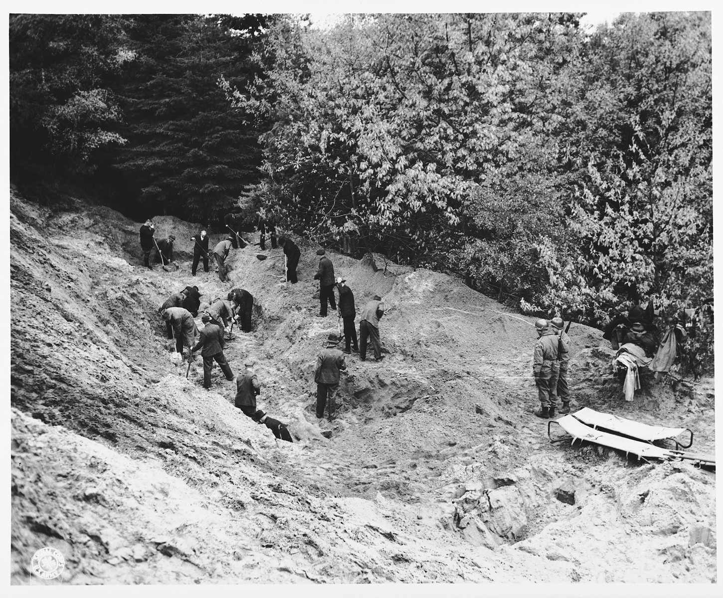 Under the supervision of American soldiers, German civilians exhume the bodies of 71 political prisoners from a mass grave on Wenzelnberg near Solingen-Ohligs.  

The victims, most of whom were taken from Luettringhausen prison, were shot and buried by the Gestapo following orders to eliminate all Reich enemies just before the end of the war.