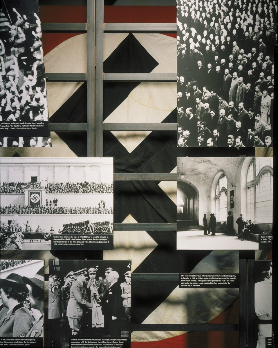 Detail of the "Nazi Society" segment in the U.S. Holocaust Memorial Museum permanent exhibition.

The segment uses photographs, film, artifacts and text to describe the Nazification of German society. The display includes a Nazi banner that once flew over Hitler's mountain retreat near Berchtesgaden in Bavaria.  In 1920, at Hitler's urging, the Nazi party adopted the swastika as its official symbol. A law passed on September 15, 1935 declared the Nazi banner to be the national flag of Germany.