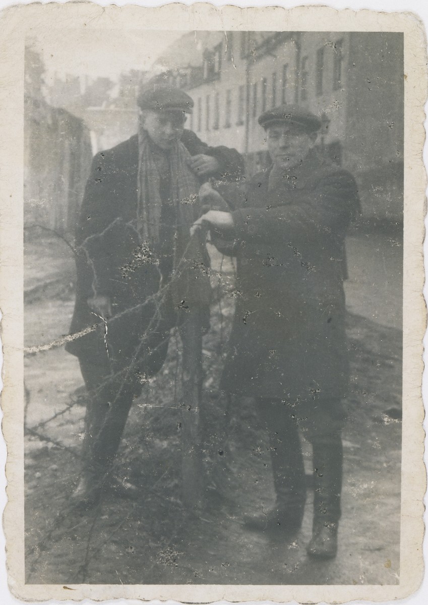 Jan Kostanski (left) and Ajzyk Wierzbicki pose on opposite sides of the barbed wire fence on Krochmalna Street that separates the ghetto from Aryan Warsaw.