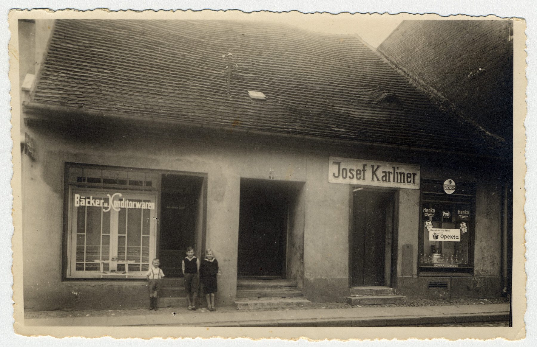 Three children pose outside the Josef Karliner grocery store.

[Pictured are probably Herbert, Walter and Ilse Karliner, the children of the store owner.]