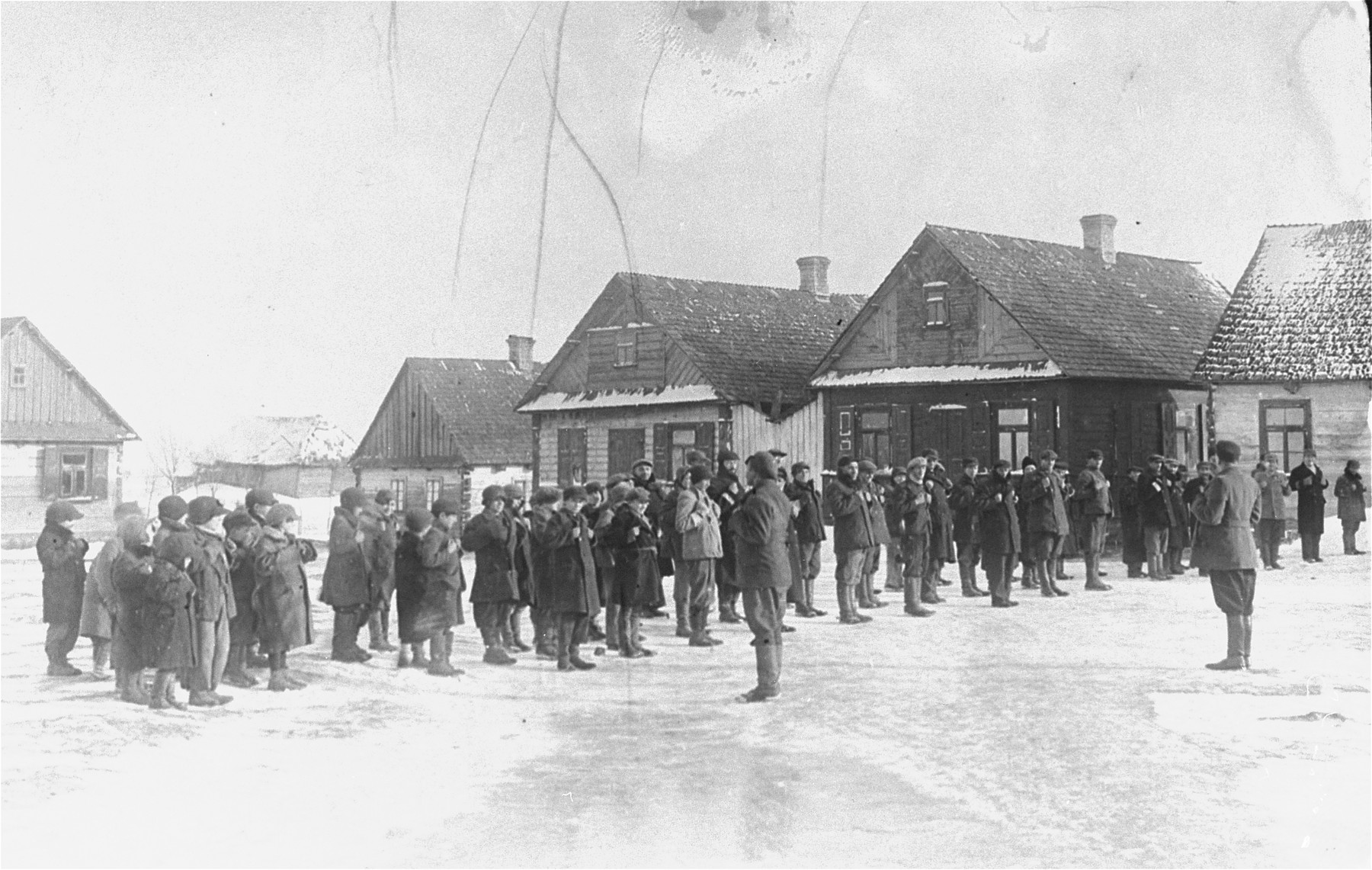 Jewish men who are lined up in an open area of the Wisznice ghetto, are forced to perform exercises.