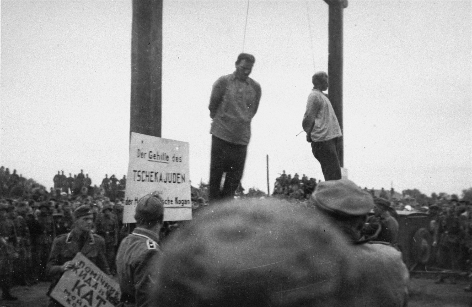The hanging of Mosche Kogan (left) and Wolf Kieper on the market square in Zhitomir.  

An SD officer is tacking up signs in Ukrainian and German that read "The assistant of the Cheka (Soviet secret police) Jew, the hangman Mosche Kogan."