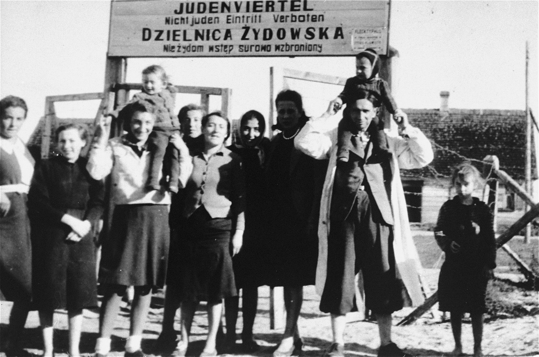 A group of Jews pose in front of the entrance to the Wisznice ghetto.  

The sign above the gate, translated from German and Polish, reads: "Jewish quarter, entrance to non-Jews is forbidden."