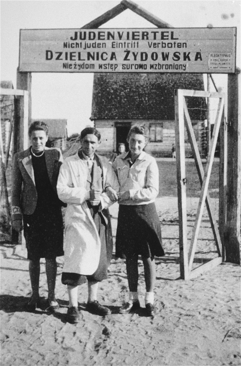 A barber and his two sisters pose at the entrance to the Wisznice ghetto.  The sign above the gate that is written in German and Polish, reads: Jewish quarter, entrance to non-Jews strictly forbidden.

The barber and his sisters were later shot by a German policeman known as Pudel.