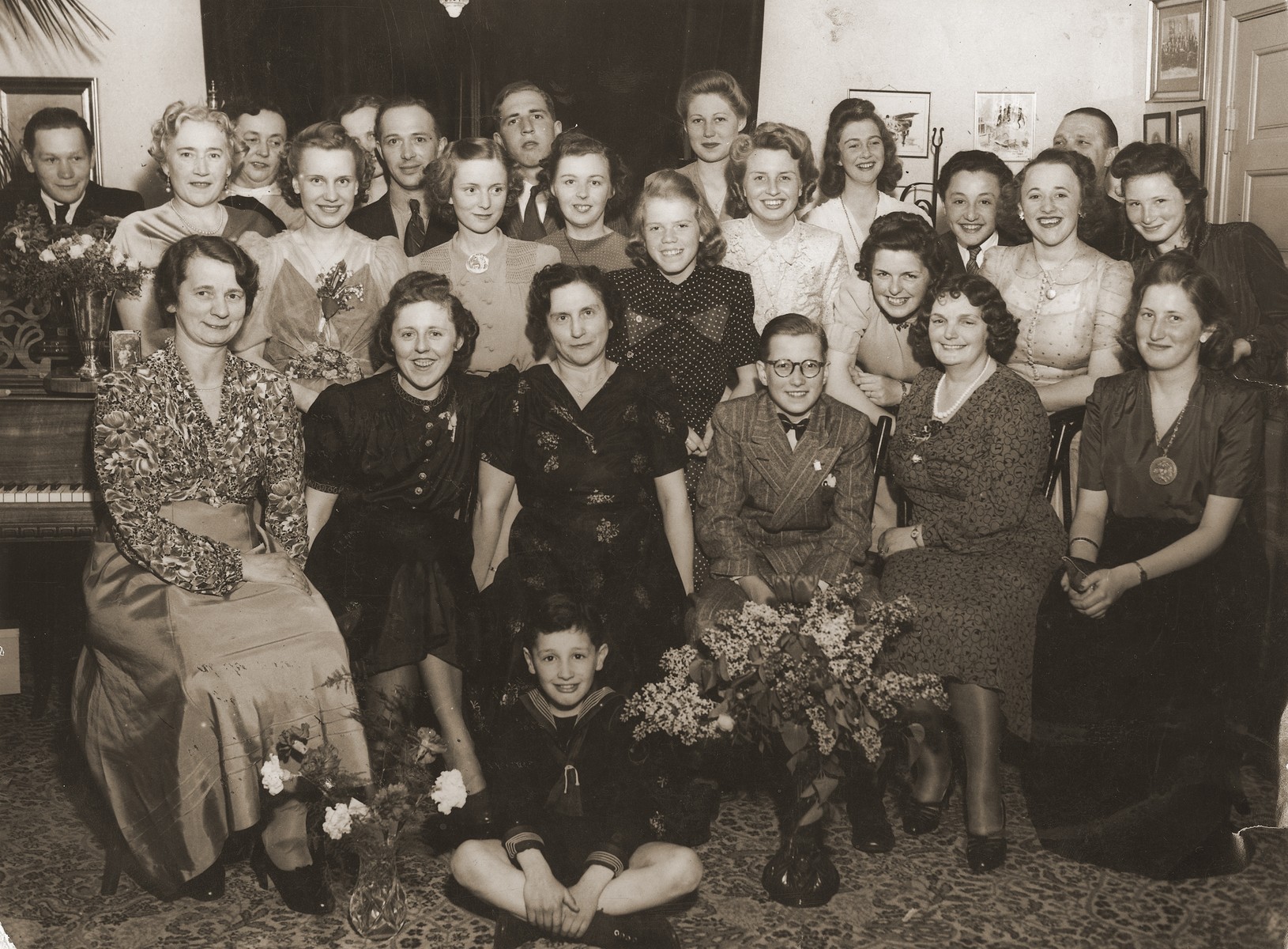 Piano students, both adults and children, pose at their piano recital.  Seated on the floor is Gus Goldberger.  Standing fourth from right is Milan Goldberger.