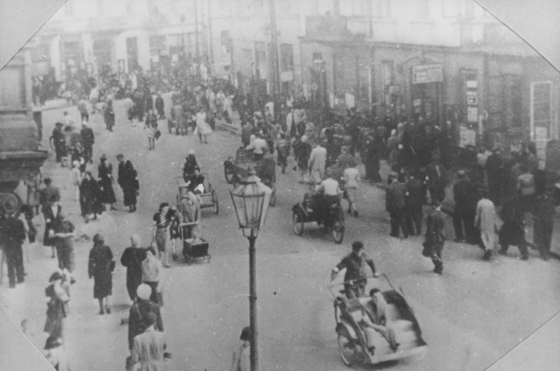 Large numbers of Jews walk and ride along a street in the Warsaw ghetto.