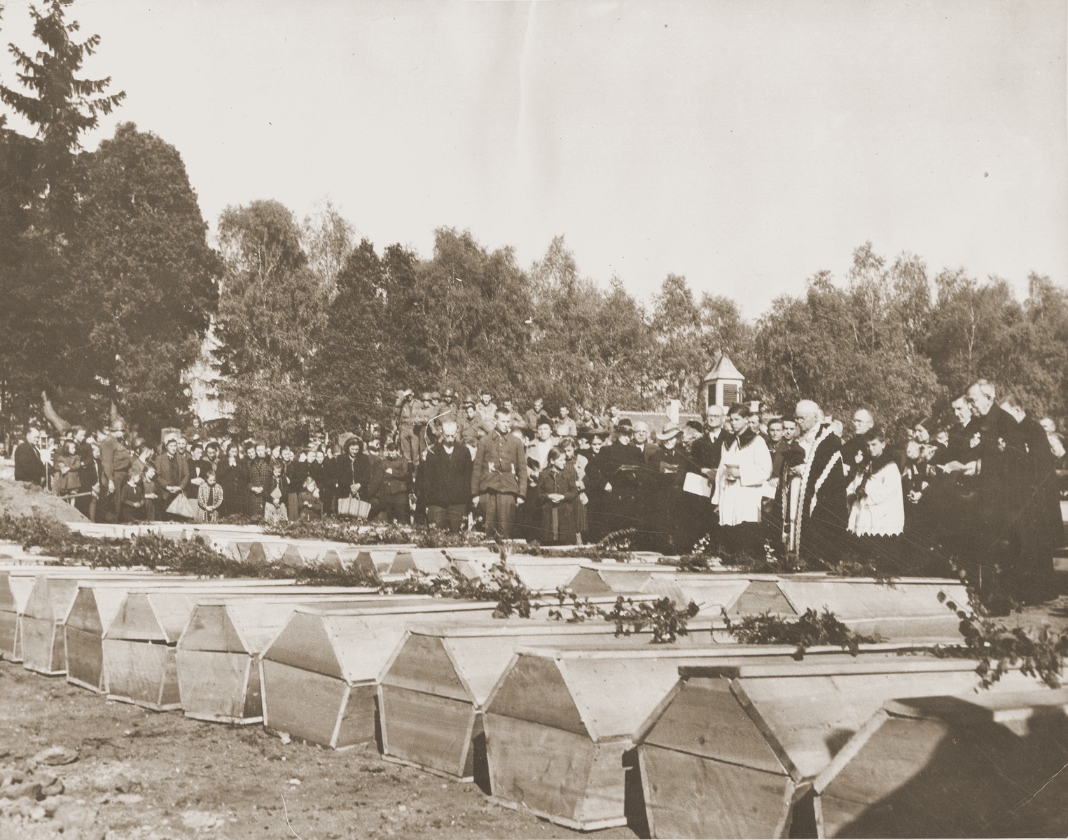 German civilians attend funeral services conducted by the pastor of Schwarzenfeld for the 140 Russian, Hungarian, and Polish Jews exhumed from a mass grave near the town.  

The victims died while on an evacuation transport from the Flossenbuerg concentration camp.

The original Signal Corps caption reads, "THIRD U.S. ARMY DISCOVERS NAZI ATROCITY.  When troops of the 26th Infantry Division, Third U.S. Army, captured Schwarzenfeld, Germany, April 22, 1945, another story of Nazi murder and atrocity was revealed.  The Americans discovered that many hundreds of helpless persons, including Allied prisoners-of-war and Polish Jewish slave laborers, had been shot in cold blood by Nazi SS troops, and their bodies thrown into a mass grave.  The executions took place on the day before the American forces captured the town.  After making official record of the circumstances, U.S. Military Government officers ordered local German civilians to exhume the bodies and provide coffins and a civilized burial for the victims.  Schwarzenfeld is 47 miles east of Nuremburg and 28 miles west of the Czechoslovakian border.

BIPPA                                                        EA 64388

THIS PHOTO SHOWS:  Approximately 500 German civilians and a group of Third Army soldiers attend burial services for the victims.  The German pastor conducting the services said local residents were unaware of the atrocity.  U.S. Signal Corps Photo ETO-HQ-45-34035.
SERVICED BY LONDON OWI TO LIST B
CERTIFIED AS PASSED BY SHAEF CENSOR